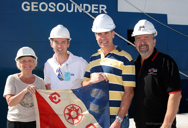 Glenys McDonald, David Mearns, John Perryman, and Mac McCarthy standing together on the deck of the Geosounder holding the Explorers Club Flag.