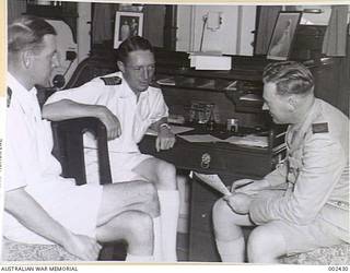 <em>SYDNEY</em> GETTING THE STORY IN THE CAPTAIN'S CABIN. CAPTAIN COLLINS, COMMANDER THRUSTON AND JOHN HETHERINGTON. (NEGATIVE BY PARER).