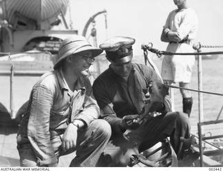 Looking at pieces of mangled iron on the deck of the cruiser HMAS Sydney II are an Egyptian engineer and Warrant Engineer Frederick William Reville RAN (right). Damage to the ship was sustained during action off Cape Spada, Crete, against the Italian vessel Bartolomeo Colleoni. Reville was killed in action when HMAS Sydney was sunk after the action with the German raider Kormoran in the Indian Ocean on 20 November 1941.