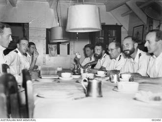OFFICERS OF HMAS SYDNEY AROUND THE TABLE IN THE OFFICERS MESS WARDROOM AT AFTERNOON TEA TIME.