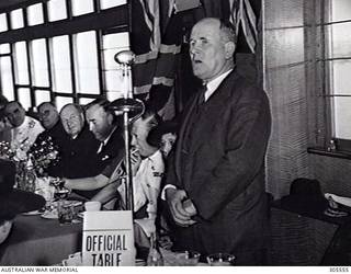 COCKATOO ISLAND DOCKYARD, SYDNEY, NSW. 1940-02-10. SIR FREDERICK STEWART, THE MINISTER FOR SUPPLY, SPEAKING AT THE LUNCHEON HELD AT THE LAUNCHING OF THE SLOOP HMAS WARREGO II. THE PRIME MINISTER, MR R. G. MENZIES IS TO THE LEFT OF THE MICROPHONE. (NAVAL HISTORICAL COLLECTION).