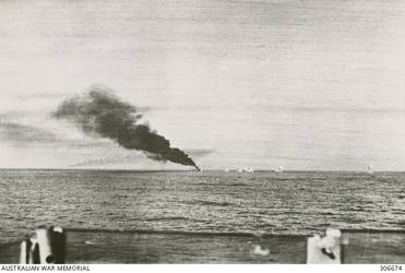SEEN FROM THE CRUISER HMAS SYDNEY (II), SHELL SPLASHES LAND NEAR THE ITALIAN CRUISER BARTOLOMEO COLLEONI DURING THE ACTION OFF CAPE SPADA. SMOKE FROM A HIT IN THE BOILER ROOM POURS FROM THE FORWARD FUNNEL OF THE ITALIAN SHIP. (NAVAL HISTORICAL COLLECTION).