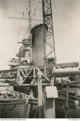 THE HOLE IN THE FORWARD FUNNEL OF THE CRUISER HMAS SYDNEY (II) VIEWED FROM THE DECK. THE DAMAGE WAS SUSTAINED IN ACTION AGAINST THE ITALIAN CRUISER BARTOLOMEO COLLEONI, OFF CAPE SPADA, CRETE, WHEN AN ENEMY SHELL EXPLODED ON THE PORT SIDE OF THE FUNNEL. (DONOR C. OLIVER, ORIGINAL ALBUM HELD IN AWM- ARCHIVE STORE)
