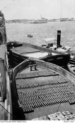 Ammunition barges moored up against the light cruiser, HMAS Sydney II, to replenish the ammunition expended during the battle of Cape Sparda. Each barge contains two types of shells, which are probably of four and six inch calibre. The rectangular shaped items in the barge (foreground) are possibly water tight covers for three pounder ammunition bins. Note the hospital ship in the background.