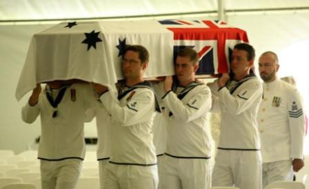 Naval pallbearers in dress uniform carry a coffin drapped in the Australian White Ensign 